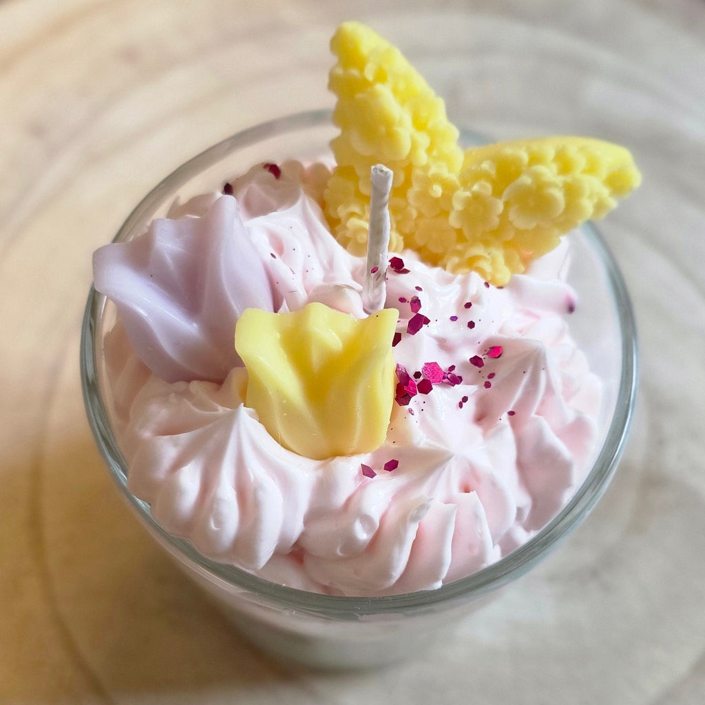 Draufsicht auf die "Tulpenwölkchen"-Duftkerze im Glas. Zu sehen ist die fluffige rosa Wachs-Haube mit handgeformten gelben Tulpen, einem gelben Schmetterling und feinen lila Glitzerpartikeln, alles aus Sojawachs. 🦋🌷