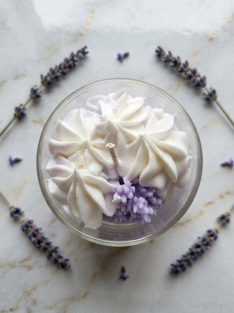 Draufsicht auf eine runde Lavendel Wölkchen handgegossene Kerze in einem klaren Glas, umgeben von einem kreisförmigen Arrangement aus getrockneten Lavendelzweigen und -blüten auf einer hellen Marmoroberfläche.