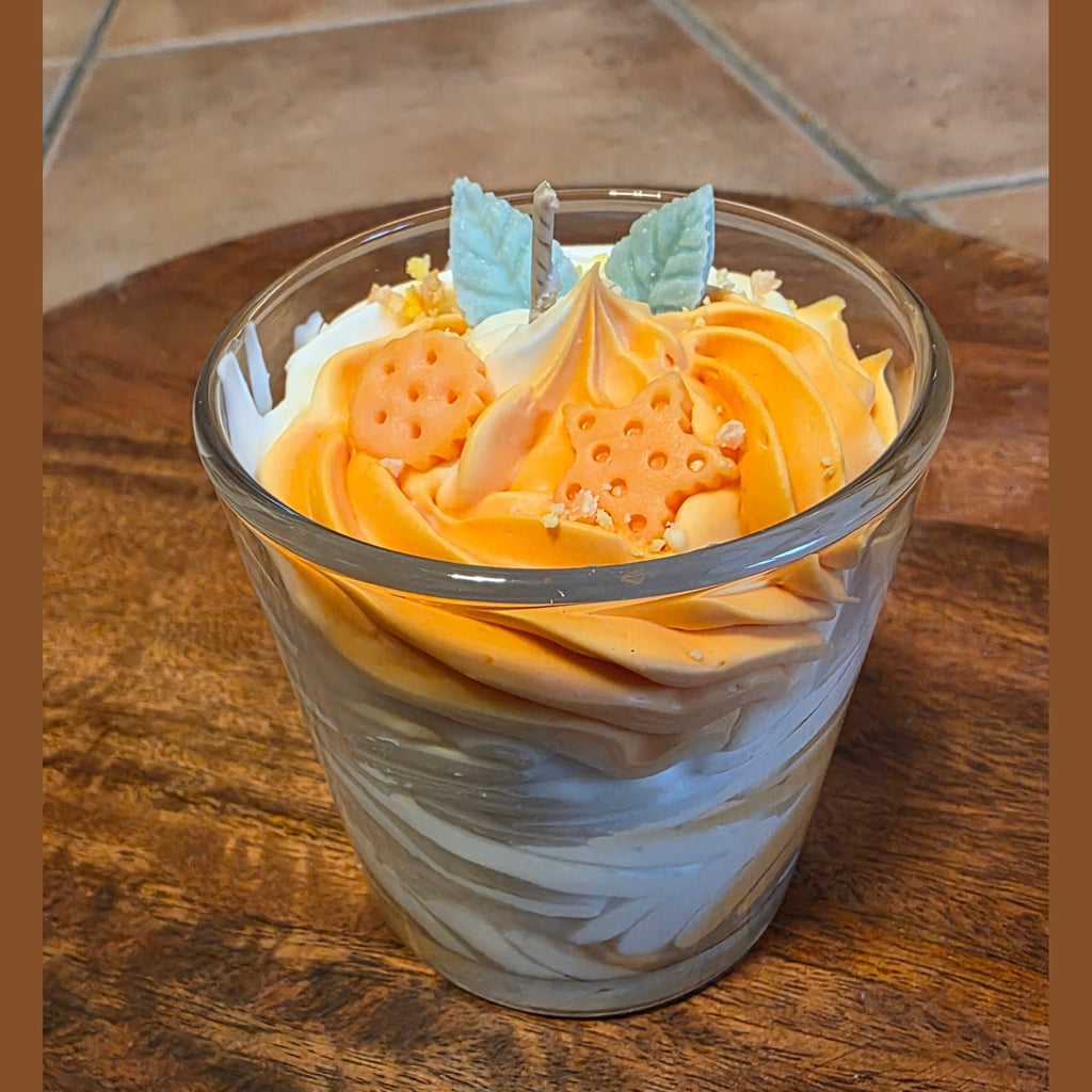 Nahaufnahme der orange-weißen Schichtkerze im Glas, die schräg auf einem runden Holztablett steht, wobei die dekorative Oberfläche mit den Wachsstücken und dem Docht gut sichtbar ist.