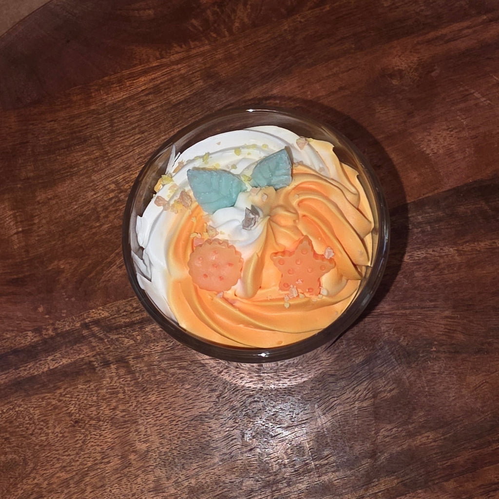 Nahaufnahme der orange-weißen Schichtkerze im Glas, die schräg auf einem runden Holztablett steht, wobei die dekorative Oberfläche mit den Wachsstücken und dem Docht gut sichtbar ist.