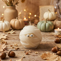 Handgemachte Sojawachskerze in Form einer weißen Mumie mit Wackelaugen im herbstlichen Setting.
