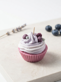 Nahaufnahme einer handgegossenen Cupcake-Kerze auf einer Holzoberfläche, verziert mit einer Sahnehaube, Beeren und einem Kerzendocht.